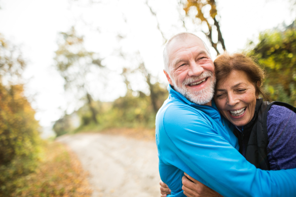 Beautiful active senior runners hugging outside in sunny autumn forest