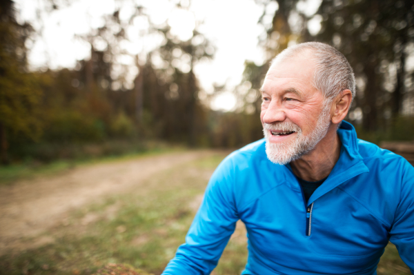 Close up of senior runner in nature. Man in blue sweatshirt, resting, smiling.