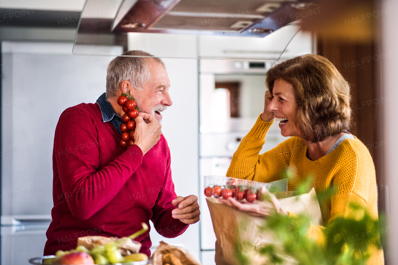 Senior couple preparing food in the kitchen. An old man and woman inside the house, having fun.