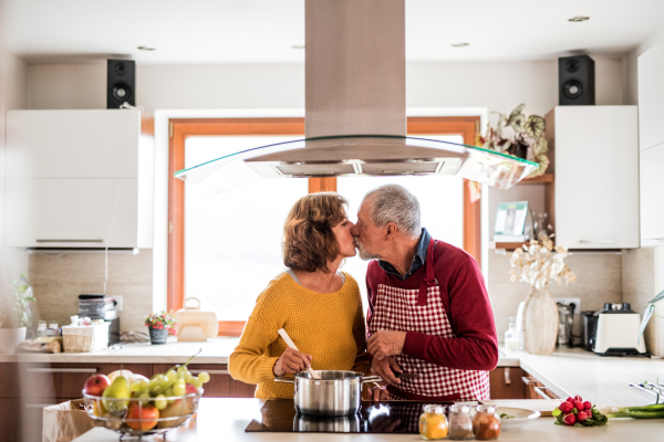 Senior couple preparing food in the kitchen, kissing. An old man and woman inside the house.