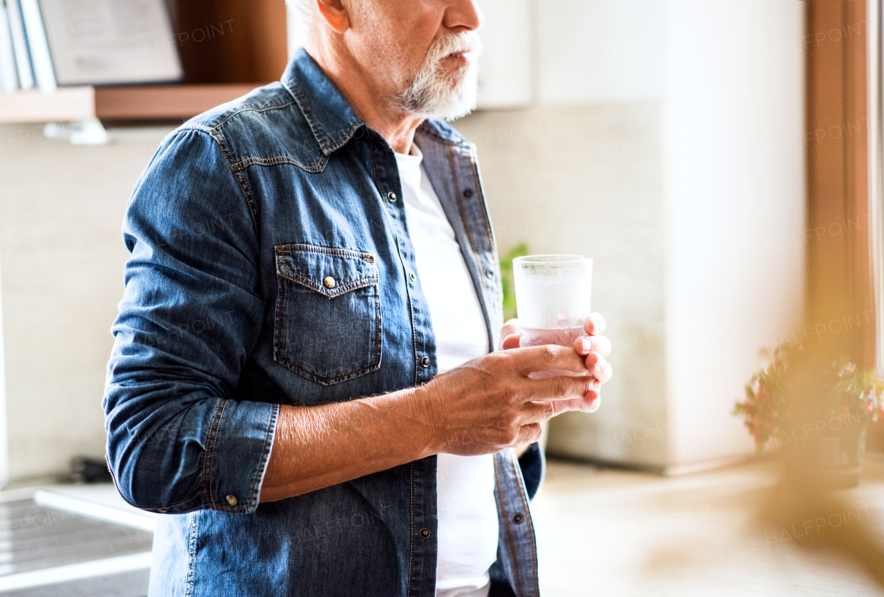 Senior man in the kitchen. An unrecognizable old man inside the house, holding a glass of water.