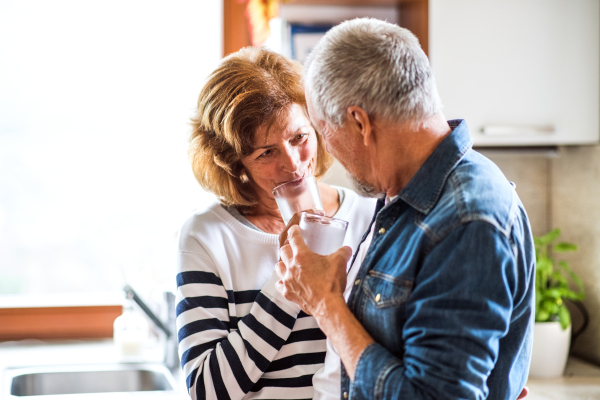 Senior couple talking in the kitchen. An old man and woman inside the house, holding a glass of water.