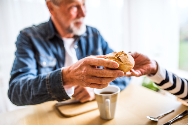 Senior couple eating breakfast at home. An old man and unrecognizable woman sitting at the table , eating breakfast.