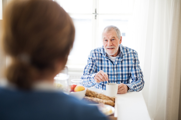 A happy senior couple sitting at the table at home, having breakfast.