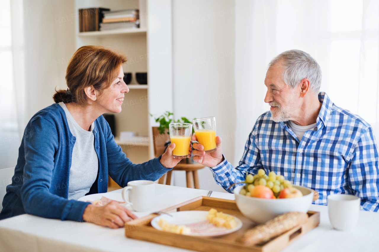 A happy senior couple sitting at the table at home, having breakfast.