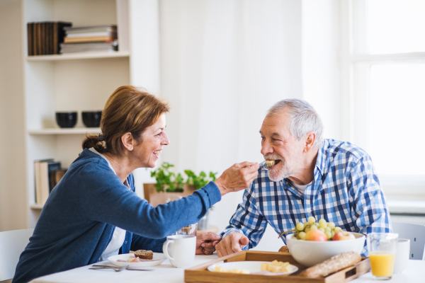 A happy senior couple sitting at the table at home, having breakfast.