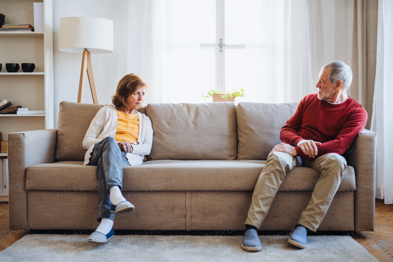 An angry senior couple sitting on a sofa at home, having an argument.