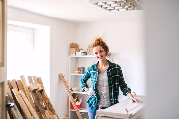 Small business of a young woman. Beautiful young woman worker in workroom. Female carpenter standing by her products.