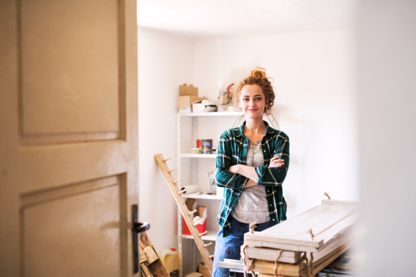 Small business of a young woman. Beautiful young woman worker in workroom. Female carpenter standing by her products, crossed arms.