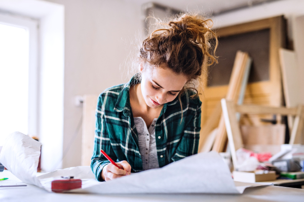 Small business of a young woman. Beautiful young woman worker in a workroom. Female carpenter sketching a project.