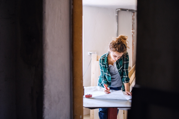 Small business of a young woman. Beautiful young woman worker in a workroom. Female carpenter sketching a project.