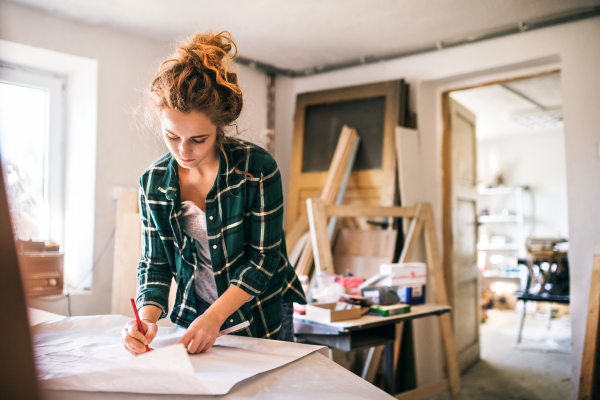 Small business of a young woman. Beautiful young woman worker in workroom. Female carpenter sketching a project.