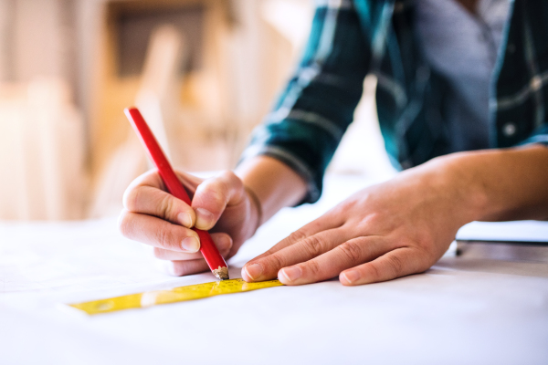 Small business of a young woman. Unrecognizable young woman worker in a workroom. Female carpenter sketching a project.