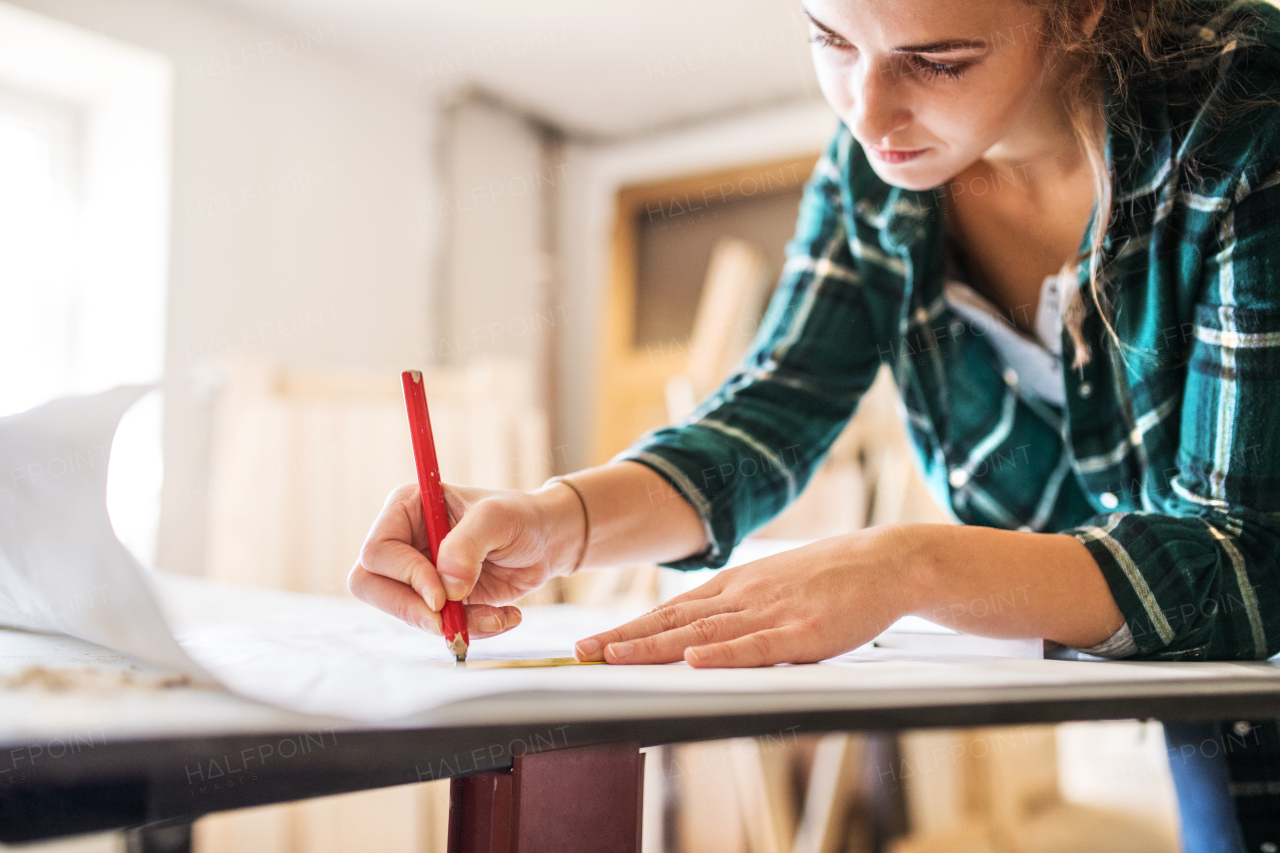 Small business of a young woman. Beautiful young woman worker in workroom. Female carpenter sketching a project.