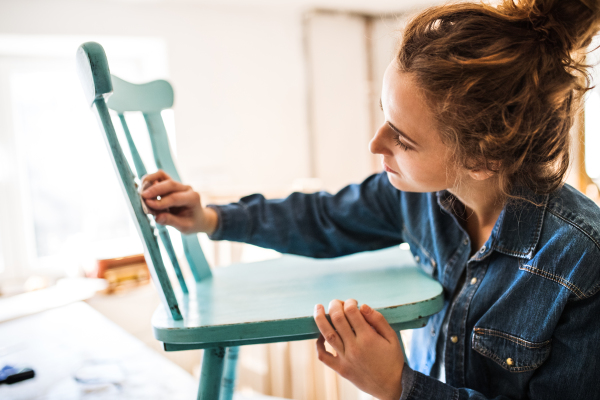 Small business of a young woman. Beautiful young woman worker in carpenter workroom. Old furniture restoration.