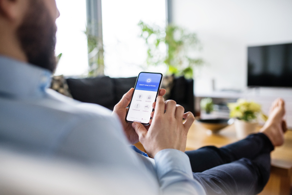 An unrecognizable man holding a smartphone with smart home control system.