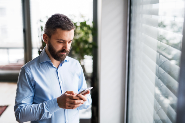 A handsome man with a smartphone by the window, text messaging.