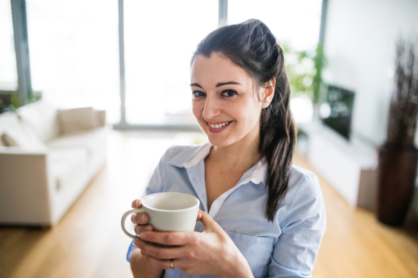 A happy woman holding a cup of coffee at home.