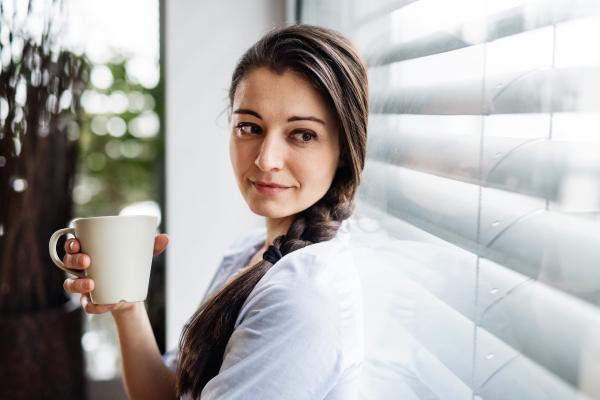 A woman sitting by the window, holding a cup of coffee.