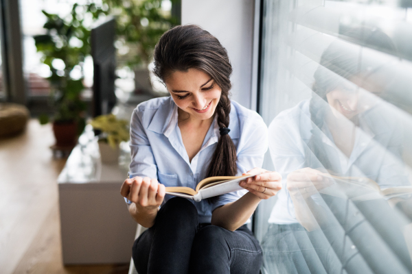 A woman sitting by the window, reading a book.