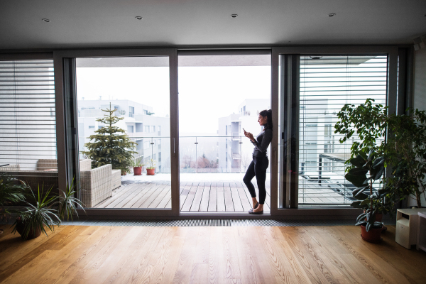 A woman with smartphone standing in an open door, text messaging.