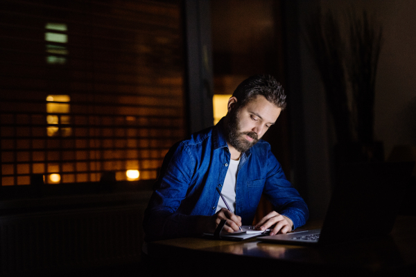 A handsome man working on a laptop at home or in an office at night.