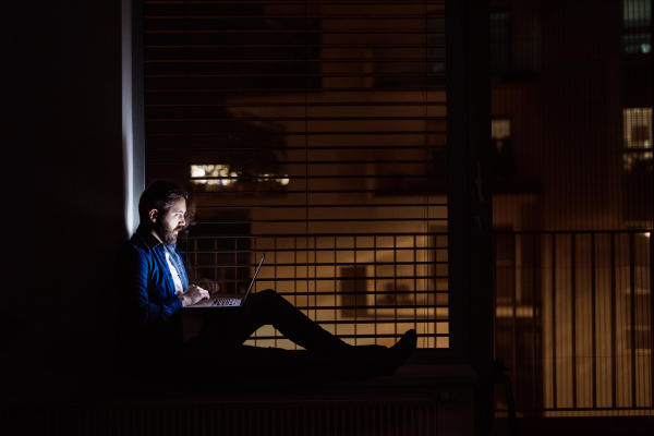 A handsome man working on a laptop at home or in an office at night.