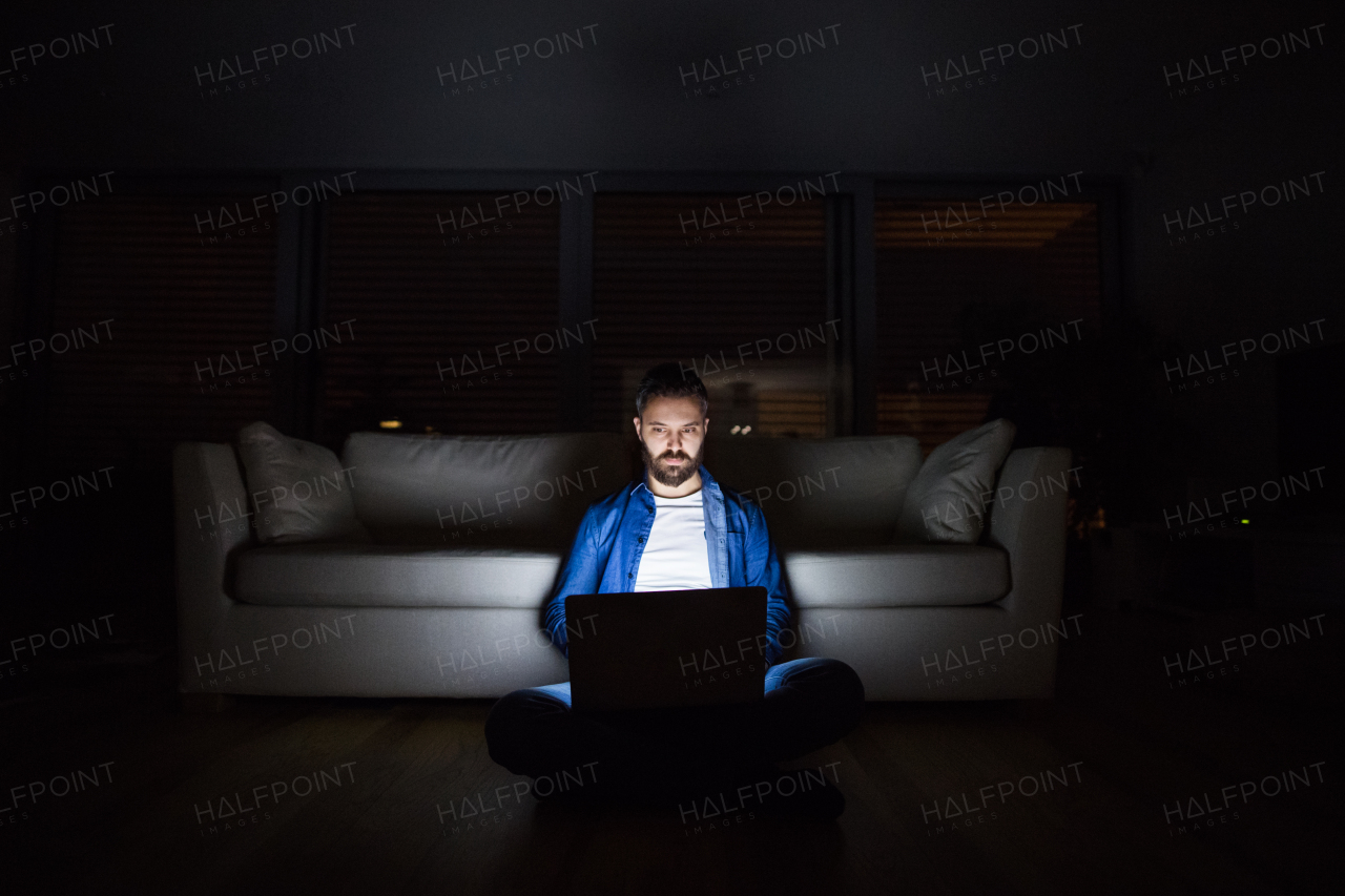 A handsome man working on a laptop at home at night.