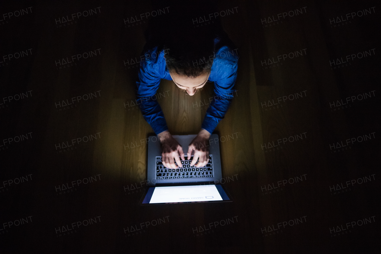 A man working on a laptop at home at night. Smart home control system. Top view.