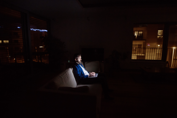 A handsome man working on a laptop at home at night.