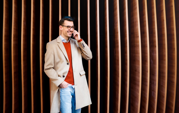 Young handsome man with smartphone standing against wooden wall, making a phone call.