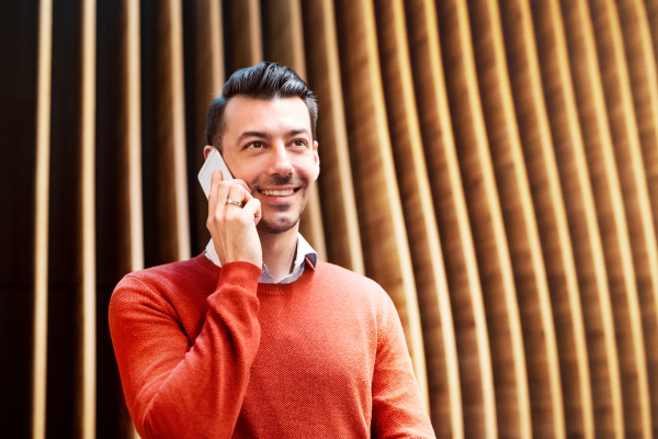 Young handsome man with smartphone standing against wooden wall, making a phone call.