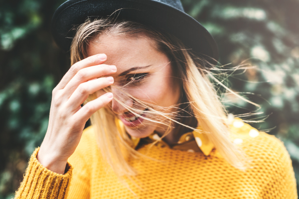 Young woman with black hat standing against a green background in sunny spring nature.