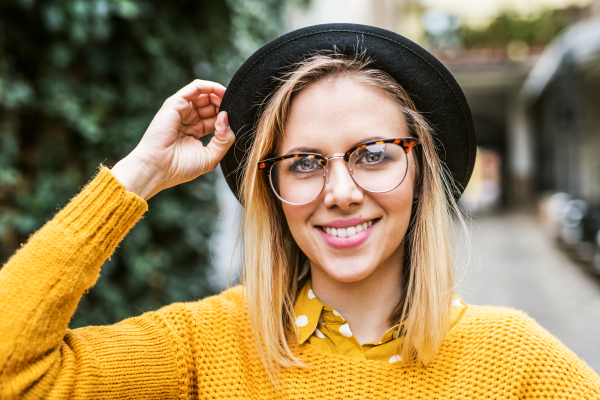 Portrait of a young woman with black hat and glasses in sunny spring town.