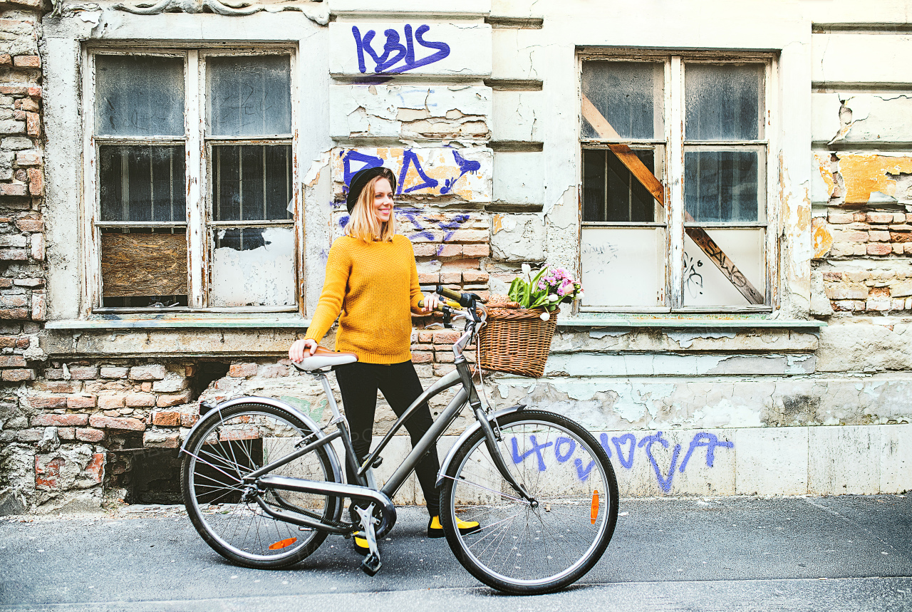 Portrait of a young beautiful woman with bicycle standing against old building. Sunny spring town.