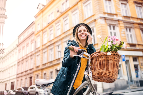 Young beautiful woman with bicycle and smartphone in town, making a phone call. Sunny spring.