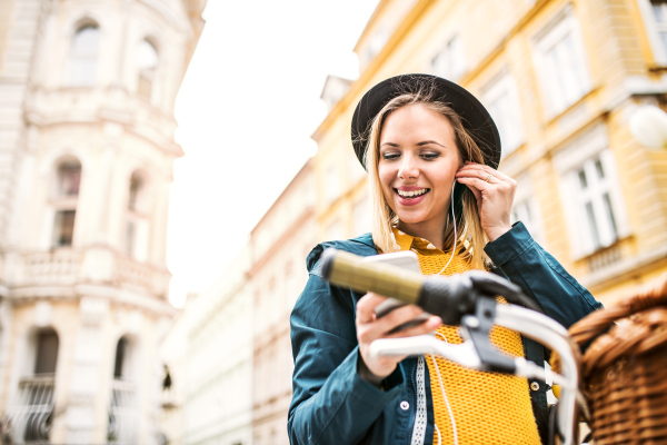 Young beautiful woman with bicycle and smartphone in town. Sunny spring.