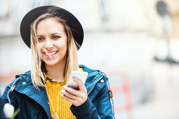 Young beautiful woman with smartphone and earphones in town. Sunny spring.