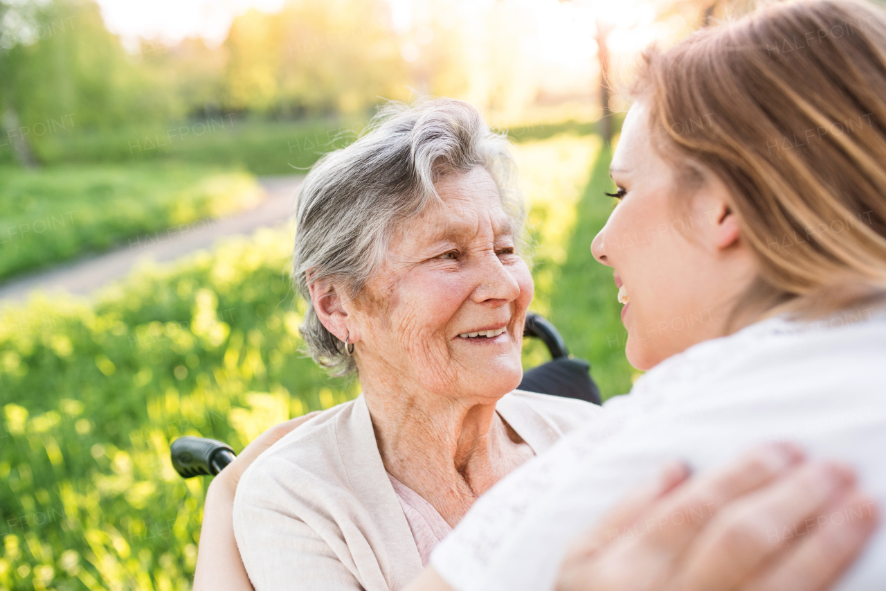 Elderly grandmother in wheelchair with an adult granddaughter outside in spring nature.