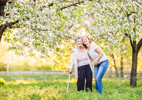 Elderly grandmother with forearm crutch and an adult granddaughter walking outside in spring nature.