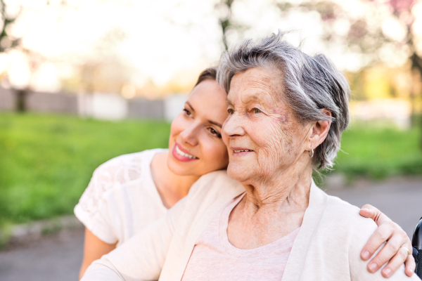 Elderly grandmother and an adult granddaughter outside in spring nature, hugging.