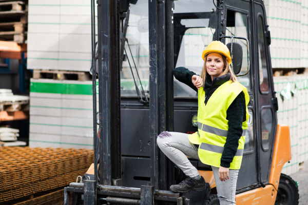 Woman forklift truck driver in an industrial area. A woman standing in front of the fork lift truck outside a warehouse.