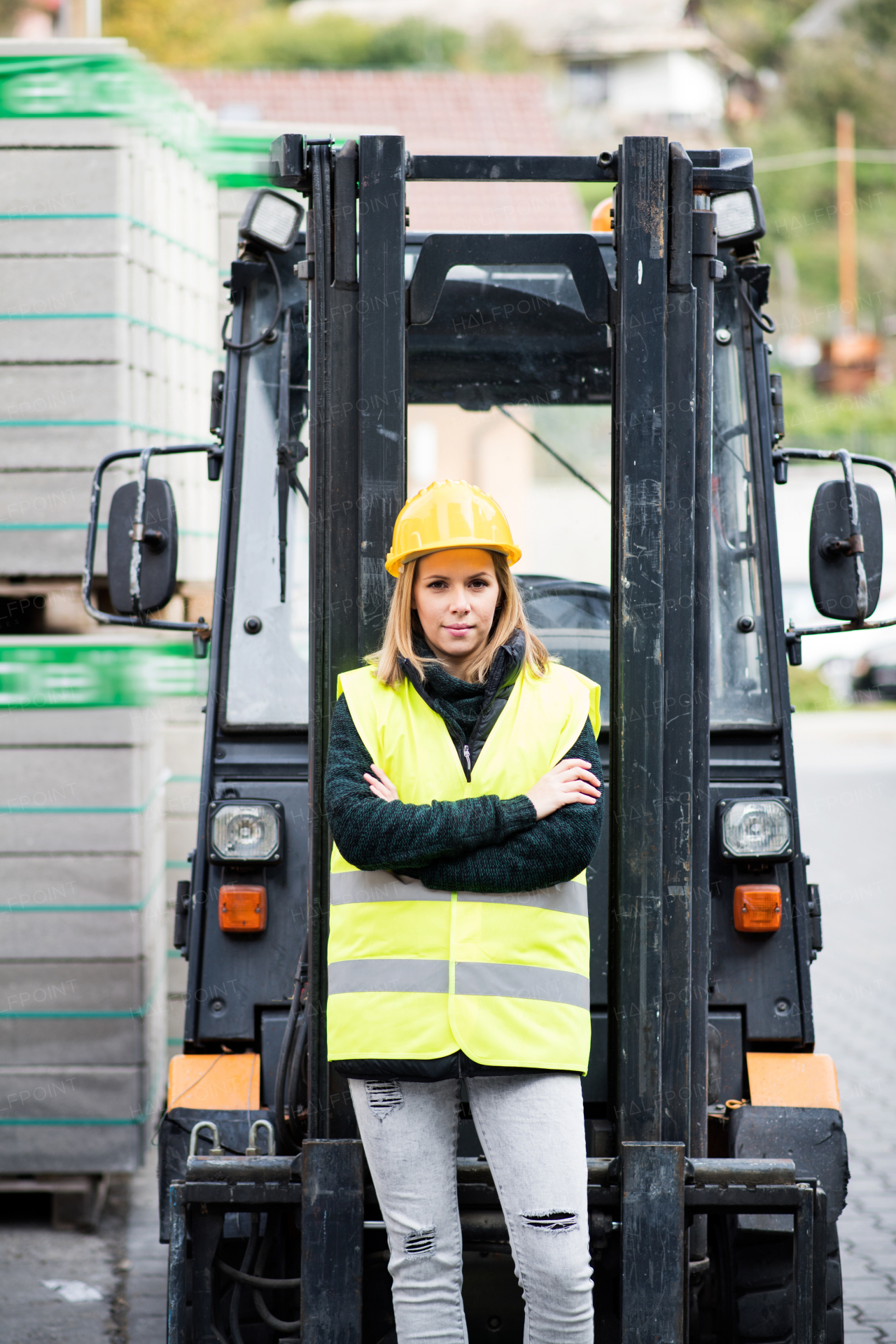 Female forklift truck driver outside a warehouse. A woman standing in front of the fork lift truck, arms crossed.