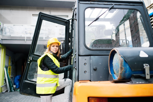 Female forklift truck driver outside a warehouse. A woman getting in the fork lift truck.