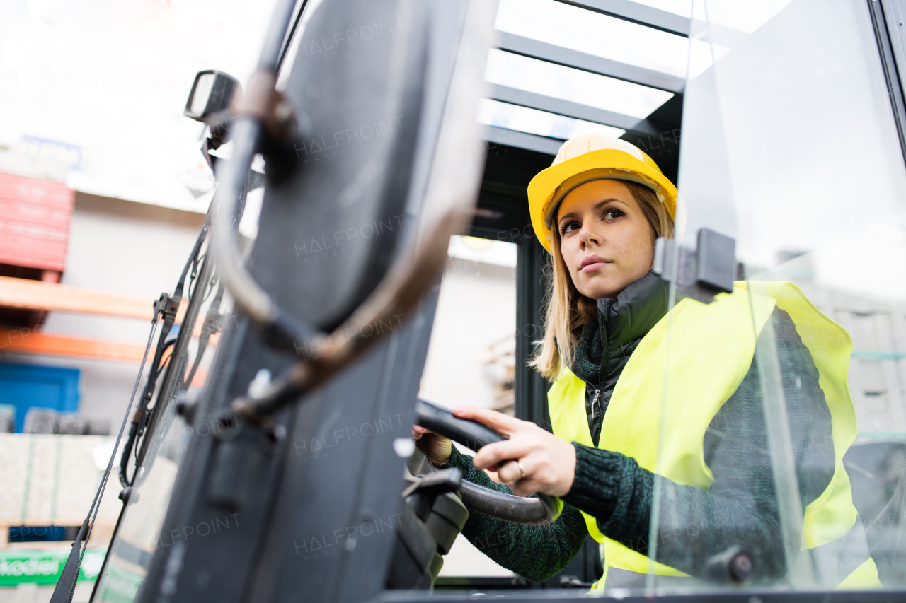 Female forklift truck driver in an industrial area. A woman sitting in the fork lift outside a warehouse.