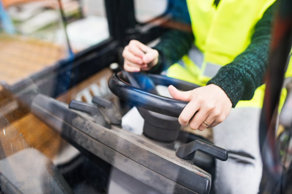 Unrecognizable female forklift truck driver in an industrial area. A woman sitting in the fork lift outside a warehouse. Shot through glass.