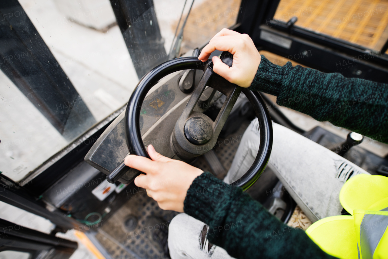 Unrecognizable female forklift truck driver in an industrial area. A woman sitting in the fork lift outside a warehouse.