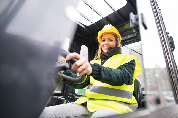 Female forklift truck driver in an industrial area. A woman sitting in the fork lift outside a warehouse.