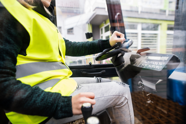 Unrecognizable female forklift truck driver in an industrial area. A woman sitting in the fork lift outside a warehouse.