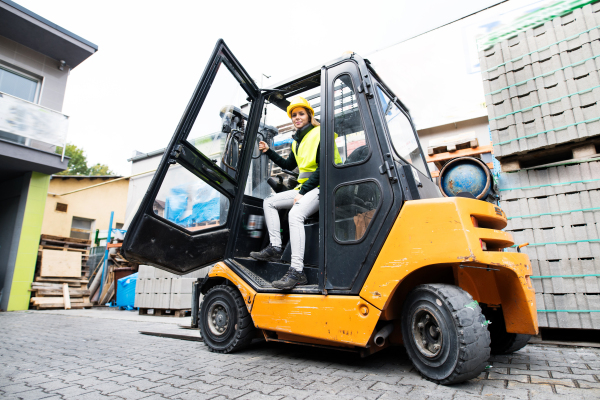 Female forklift truck driver outside a warehouse. A woman getting out of the fork lift truck.